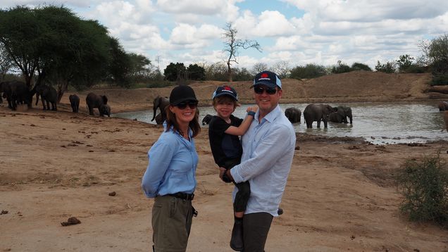 Murray with his parents in front of a watering hole in Kenya, surrounded by elephants