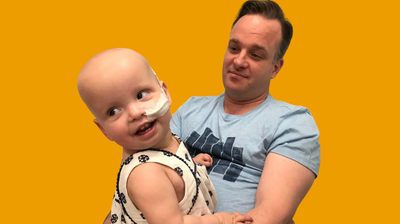 Adelaide being held by her father, medical tubing in her nostril for cancer treatment