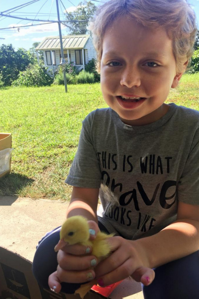 Millie sits smiling in the backyard on a sunny day, proudly wearing a t-shirt with the slogan 