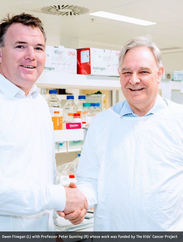 While in a research lab, Owen and Professor Peter Gunning shake hands while smiling for the camera.