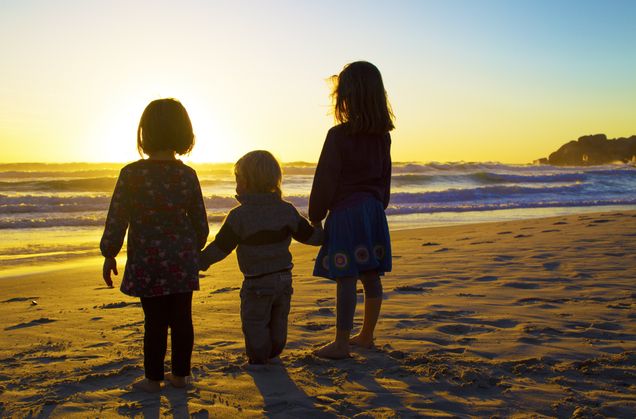 Murray as a little boy on the beach facing the ocean as the sun sets with his sisters Phoebe and Stella on either side of him holding his hands