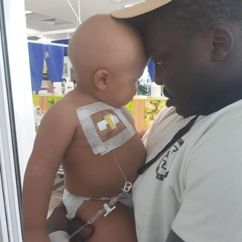 CJ and his Dad, Callisto, share a gentle hug in the hospital ward; CJ has a port on his chest to receive his cancer treatment.