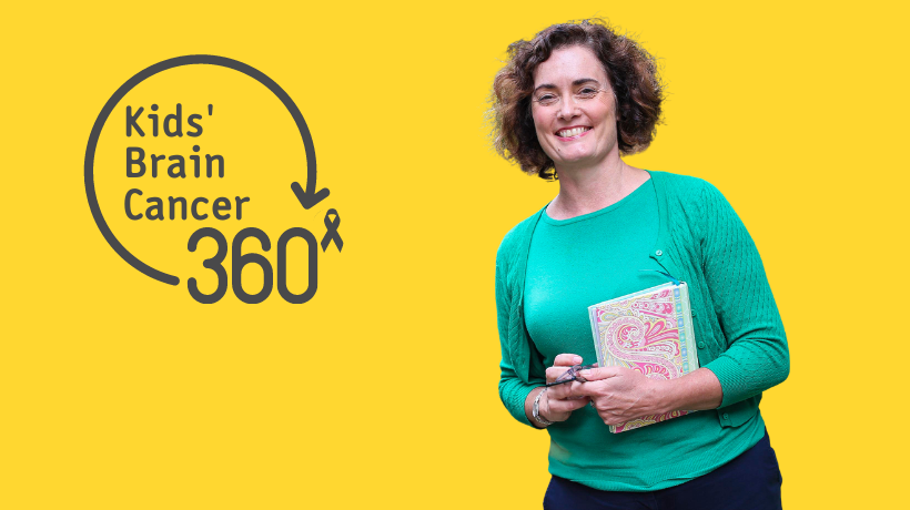 Suzanne Momber smiles for the camera holding a colourful notebook - the bright yellow backdrop contrasts with her vivid green top and cardigan; to the left is the Kids' Brain Cancer 360 logo.