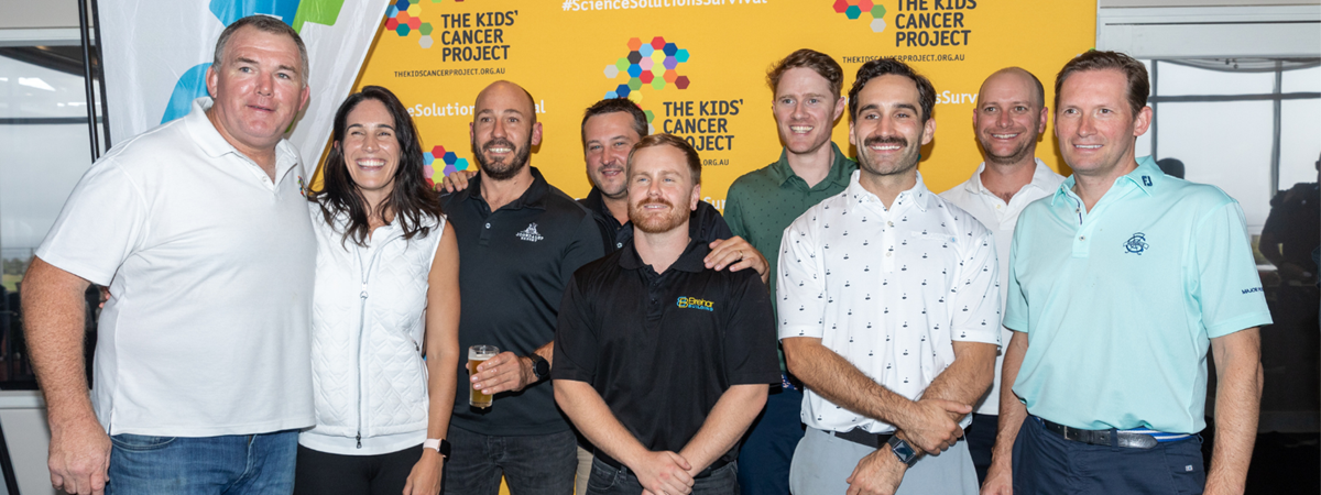 A large group photo of Owen Finegan and other participants in the charity golf event - they are all smiling and standing in front of a large banner with TKCP branding on it.