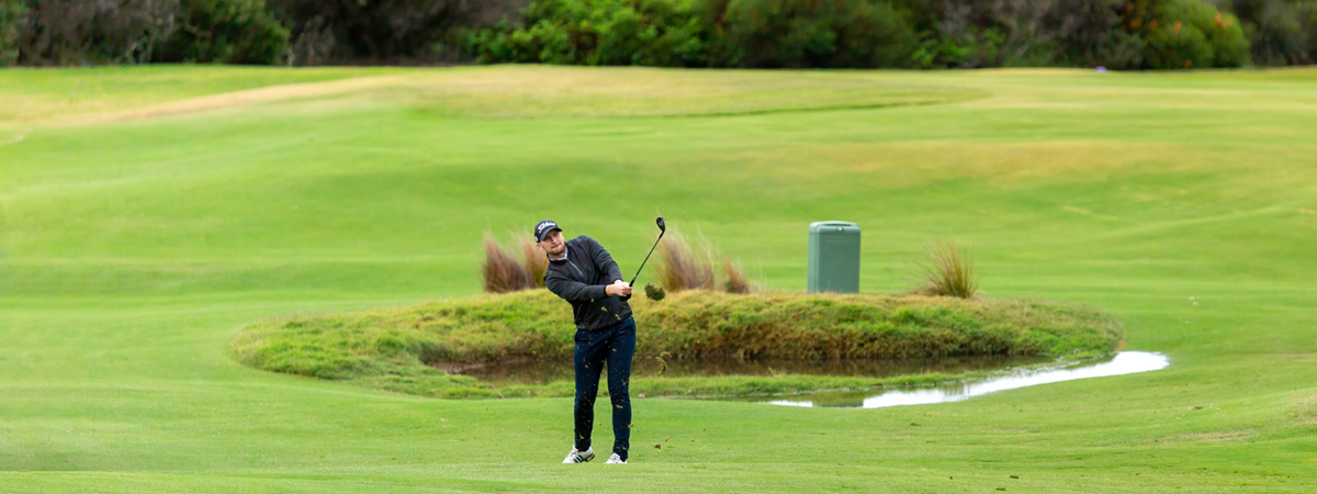 A golfer stands on the fairway of the course and takes a swing.