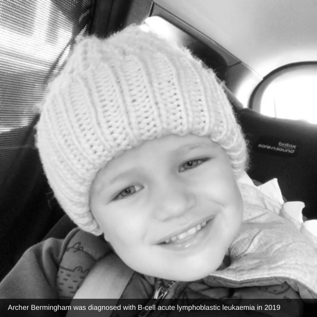 In a black and white photograph, Archer smiles for the camera while wearing a warm, knitted beanie; below are the words: 