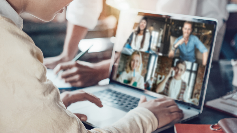 The image depicts an office environment where a worker is collaborating with colleagues via videoconference.