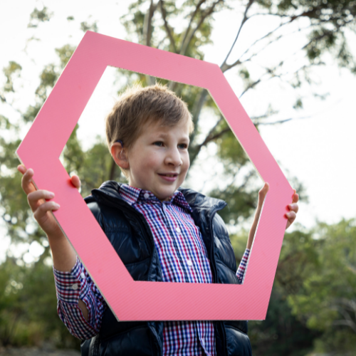 A boy holding a pink hexagon to frame his face