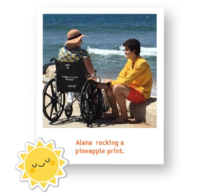 Alana in a wheelchair at the beach wearing a pineapple print t-shirt