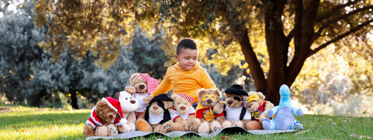 CJ sits on a picnic rug in a park, proudly displaying his collection of TKCP bears in a row.