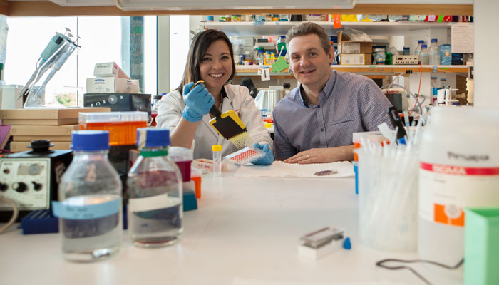 Dr Raelene Endersby and Professor Nick Gottardo are sitting in a lab surrounded by clinical testing equipment; they smile as they perform their important work.