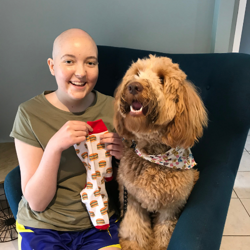 Lexie sitting next to a dog, holding a pair of socks in a burger print