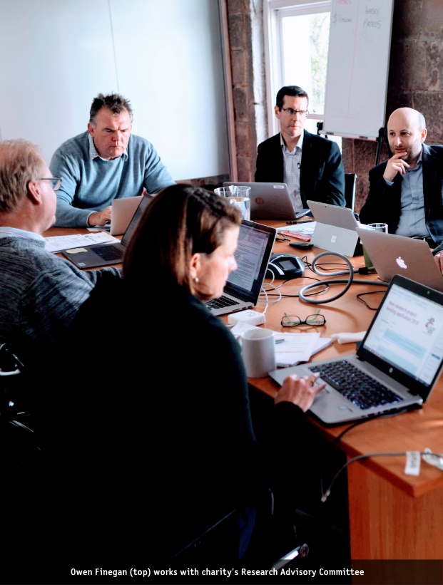 Owen sits at the head of a boardroom table as the Research Advisory Committee hold a meeting.