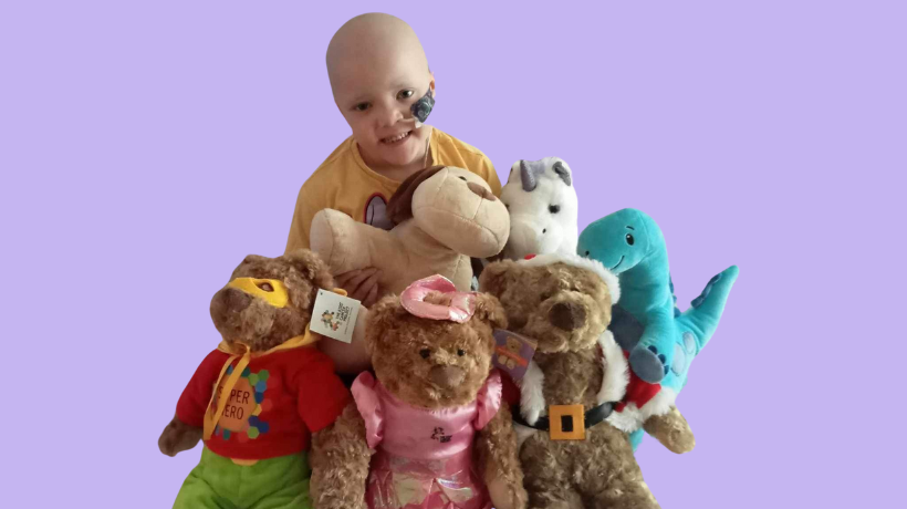 Maia is pictured cuddling with a variety of TKCP bears; she is smiling despite the challenges of her cancer treatment.