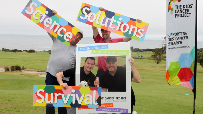 Four men dressed in their golfing attire holding signs in support of The Kids' Cancer Project