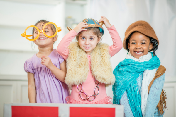 3 preschool aged children giggle and smile for the camera as they show off their creative dress-up costumes.