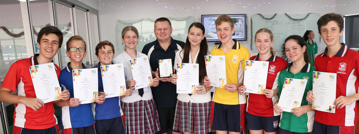 A group of students and their teacher smile while holding their participation awards for their contributions to the Write a Book in a Day event.