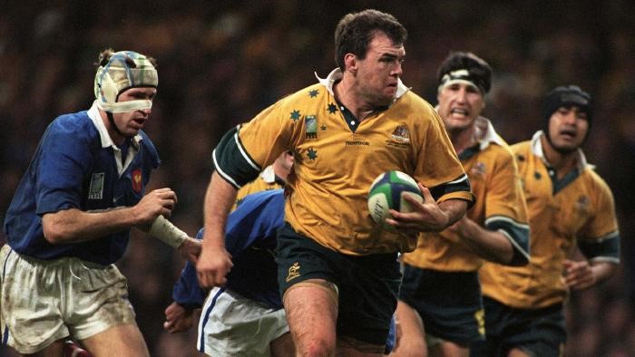 An action shot of Owen wearing his green and gold Wallabies uniform in possession of the ball during an energetic rugby match.